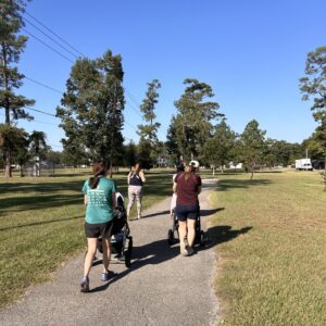 Three people walking on a paved path in a park two have strollers